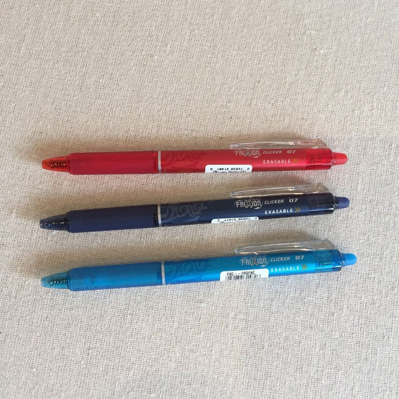 Three gel erasable pens in red, blue, and black colors, displayed on a textured surface.