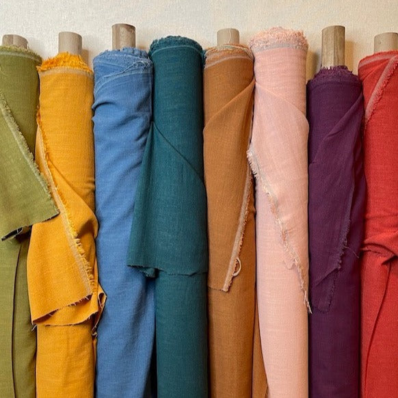 Silky rayon linen slub fabric for apparel sewing. A group shot of several colorways of this viscose linen blend, including seaweed, amber, dark denim, hunter, brown, bulsh, plum and rust. 